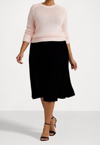 Světle růžový pletený svetr s žebrovanými manžetami a spodním lemem, kombinovaný s černou sametovou sukní ve tvaru A a černými sandály na podpatku se stahováním.