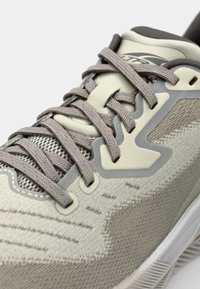 Light gray athletic shoe with textured fabric upper, mesh accents, and gray laces. Notable design features include a shaped overlay and rubber sole.