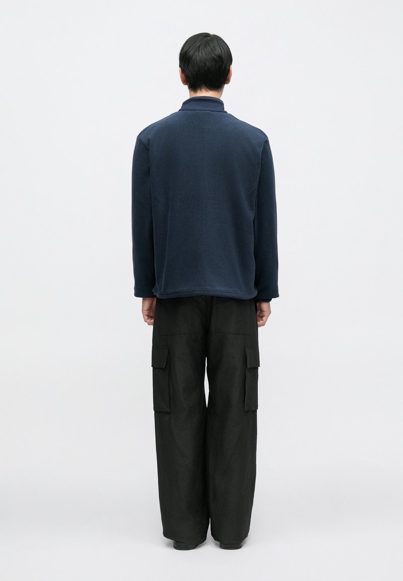 Haut bleu marine à col montant et manches longues, associé à un pantalon cargo noir ample avec des poches plaquées.