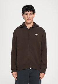 Brown zip-up hoodie made from textured fabric, featuring a hood, ribbed cuffs, and a small logo on the left chest.