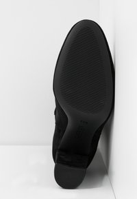 Černé semišové kotníkové boty s vzorovanou černou gumovou podrážkou; mají kulatou špičku a silný podpatek pro stabilitu.