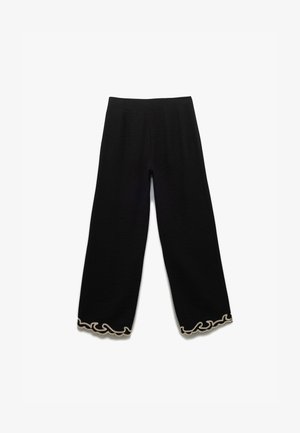 Schwarze weit geschnittene Hose aus strukturiertem Stoff, mit einer gewellten weißen Borte am Saum. Elastischer Bund für zusätzlichen Komfort.