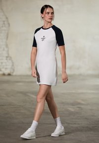 Kortermet kjole i hvit med marineblå raglanermer, med "tommy girl" logo. Brukt med hvite sneakers og sokker, som fremhever et avslappet utseende.