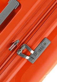 Valigia arancione con guscio rigido, doppie zip e lucchetto combinato. Presenta dettagli testurizzati e una finitura superficie liscia.