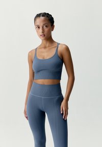 Modrý atletický krátký top s žebrovanou strukturou a tenkými ramínky, doplněný o odpovídající legíny s vysokým pasem, které mají vertikální texturu a detaily švů.