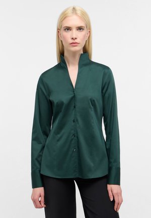 Donkergroene overhem shirt met opstaande kraag, lange mouwen en een gladde satijnen textuur. Voorzien van knopen aan de voorkant en een aansluitende pasvorm.