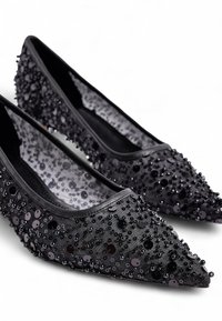 Zapatos planos negros con lentejuelas y puntera puntiaguda, con una tela texturizada adornada con cuentas y lentejuelas, creando un detalle de superficie brillante.