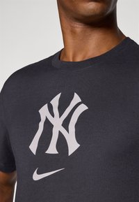 Dark gray cotton T-shirt featuring a large white New York Yankees logo and a small white Nike swoosh logo on the lower side.