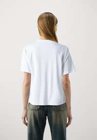 White cotton t-shirt with short sleeves, round neckline, and a relaxed fit. Paired with faded blue jeans featuring back pockets.