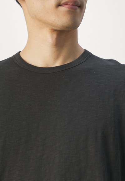 Black crew-neck t-shirt made of soft, textured fabric. Short sleeves and a relaxed fit, featuring minimal seams and no embellishments.