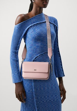 Sac en cuir rose à porter en bandoulière, avec une finition lisse, un rabat de fermeture et un logo. La sangle présente une couleur grise contrastante avec une inscription.