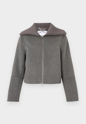 Pelēka jaka ar rāvējslēdzēju un ribaina apkakli. Piedāvā garas piedurknes un īsu dizainu. Izgatavota no mīkstas, teksturētas vilnas maisījuma auduma.