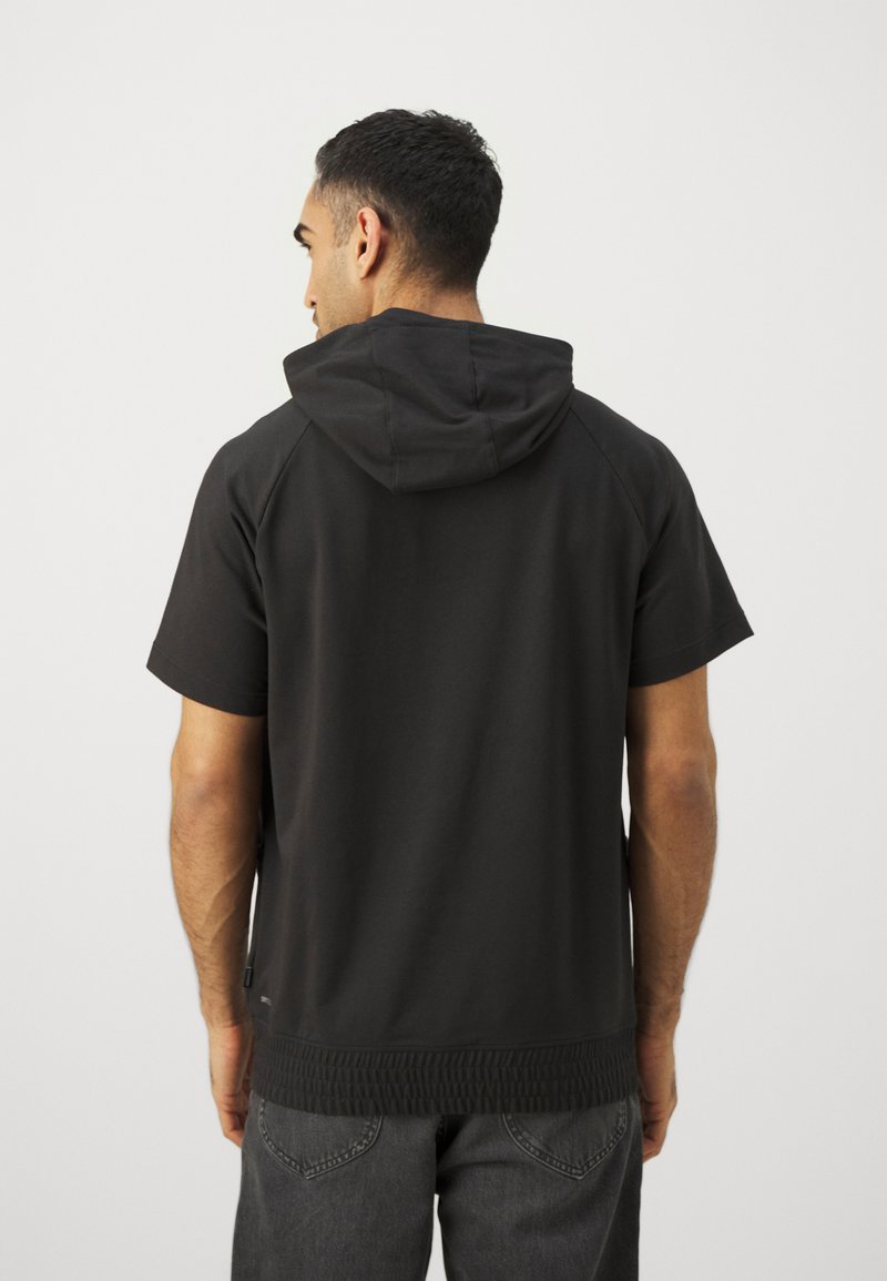 Sudadera corta negra con mangas cortas y capucha con cordones, dobladillo texturizado y mangas raglán, combinada con jeans oscuros.