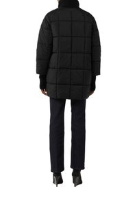 Czarna kurtka puchowa z wysokim kołnierzem, charakteryzująca się pikowanym wzorem i długimi rękawami. Połączona z ciemnymi dżinsami i szpilkami.