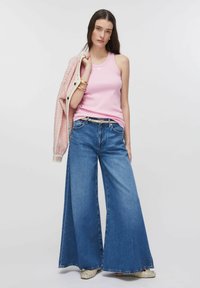 Débardeur rose clair côtelé associé à un jean en denim bleu à jambes larges, une ceinture ajustée et une veste rose texturée. Ballerines à la mode avec des ornements.