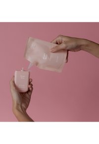 Limpiador de manos Bright Rose en una suave botella rosa se está rellenando desde un pouch a juego. Ambos presentan texto blanco minimalista en el envase.