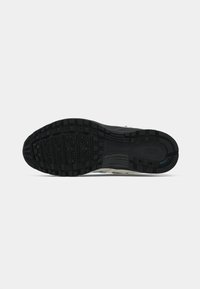 Melna gumijas zole sporta apaviem ar kvadrātu rakstu un Nike logo, aplūkojot no apakšas uz balta fona.