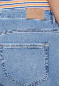 Light blue denim jeans with a rectangular brown leather tag labeled "ONLY CARMAKOMA." Features a back pocket with subtle stitching.