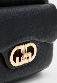 Borsa a mano in pelle nera con finitura testurizzata, caratterizzata da una chiusura in metallo color oro con incisione "GAUDI", che presenta una forma rettangolare.