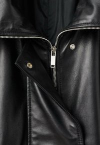 Chaqueta de cuero negro con cierre de cremallera diagonal, botones de presión y textura suave. Incluye un forro interno en contraste.