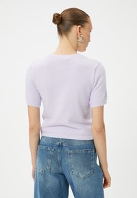 Helllila kurzärmliger Pullover mit weicher Struktur, gerippter Saum, getragen zu hellblauen hochgeschnittenen Jeans mit Gesäßtaschen.