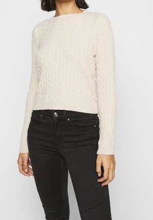 Pull en tricot crème avec un col rond et des manches longues, doté d'un ourlet et de poignets côtelés. Associé à un jean noir ajusté.