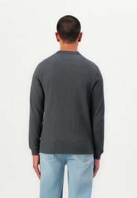 Cămașă pulover cu mâneci lungi, de culoare gri cărbune, cu o textură canelată și guler rotund, completată cu blugi largi de culoare albastru deschis.