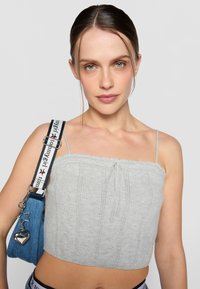 Grå strikket crop topp med tynne stropper, med teksturerte mønstre og snor detalj foran. Kombinert med en blå skulderveske.