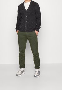 Černý strukturovaný cardigan s výstřihem do V a šesti knoflíky, doplněný o zelené chinos kalhoty a šedo-bílé tenisky. Neformální outfit pro muže.