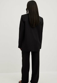 Mustajad tailored bleiser ja laiad püksid siledast kangast, millel on mugav lõige ja sirge siluett, vaadatuna selja tagant.