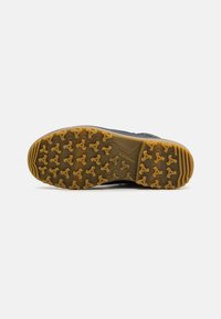 Black footwear sole with a thick gum-colored tread featuring triangular lugs for traction, marked with “LOWA” on the side.
