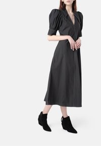 Czarna sukienka o średniej długości z krótkimi bufkami, głębokim dekoltem w kształcie litery V oraz subtelnym kontrastowym przeszyciem. Stylizowana z czarnymi botkami za kostkę.