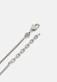 Chaîne en métal argenté avec un fermoir en homard et une petite étiquette en forme de diamant marquée "FOSSIL", présentant à la fois des maillons et des designs texturés.