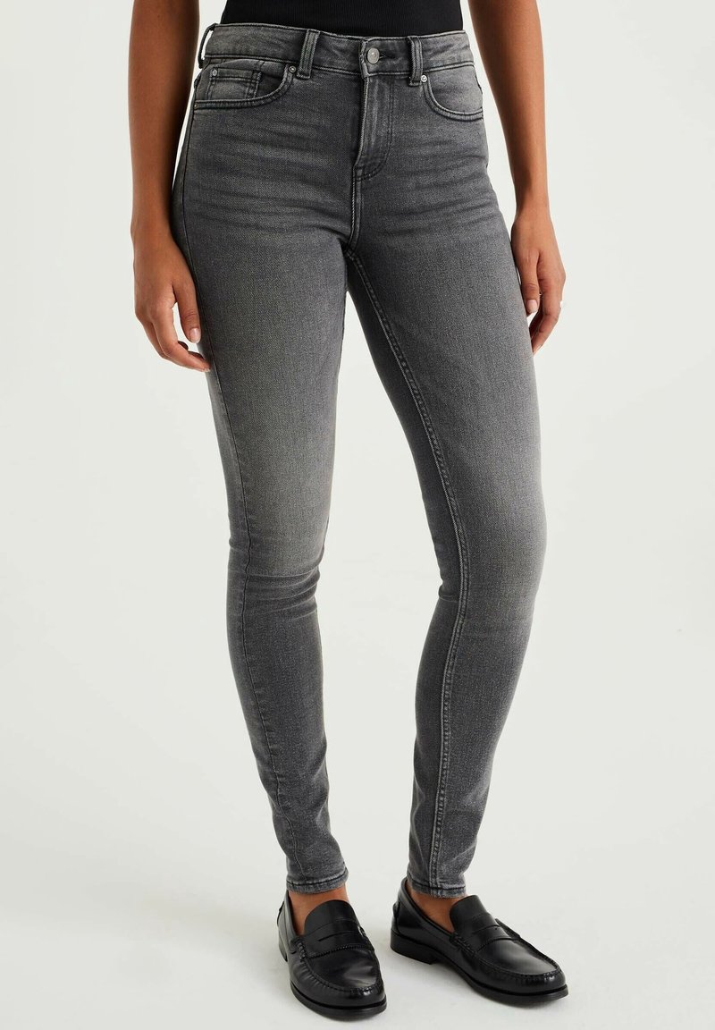 Jeans ajustados grises de mezclilla, con una cintura de altura media, cinco bolsillos y un ligero desgaste para dar textura. Combinados con mocasines negros.