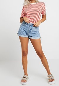 Červené a bílé pruhované tričko s kulatým výstřihem, doplněné o světle modré džíny s vyhrnutými lemy. Oblečeno s lehkými sandály.