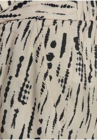 Tessuto beige con motivo astratto a traccia di pennello nero, caratterizzato da una cucitura diagonale e pieghe sovrapposte.