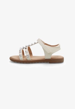 Weiße flache Sandale mit drei mit Nieten besetzten Riemen über dem Fuß, einem Klettverschluss am Knöchel und einer braunen strukturierten Sohle.