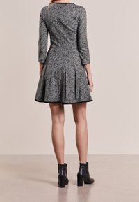 Robe à motif pied-de-poule gris avec manches longues, jupe plissée et bordure noire. Associée à des bottines noires. Texture lisse, taille ajustée.