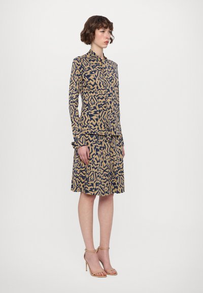 Patterned dress in beige and navy with a tailored fit, long sleeves, and a collar, featuring a geometric design and pleated skirt.