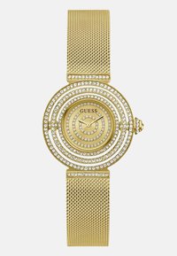 Zlatni mrežasti sat s kružnim brojčanikom okruženim dvjema vrstama sjajnih kristala. Ima minimalističko lice s jednostavnim oznakama sati.