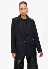 Zwarte blazer met een notch-lapel, enkele knoopsluiting, twee voorzakken en een getailleerde pasvorm. Glad materiaal en gestructureerd ontwerp.