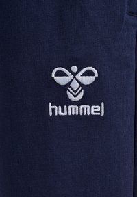 Marineblaue Sportshorts mit einem gestickten weißen Hummel-Logo, die einen glatten, elastischen Stoff und eine enganliegende Passform zeigen.