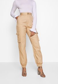 Beige cargobyxor i lätt tyg, med hög midja, två sidofickor och elastiska muddar. Matcher med en vit långärmad topp.