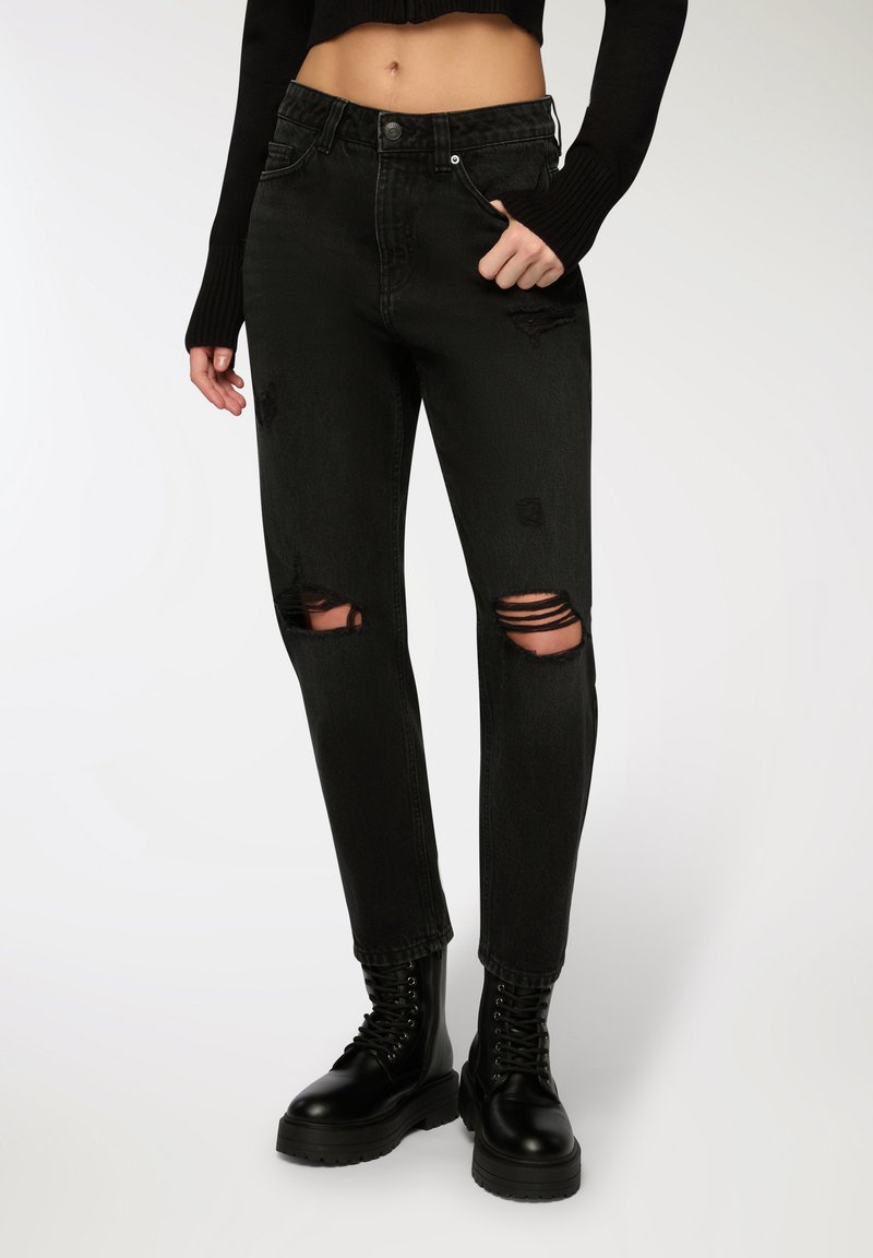 Czarne dżinsy o średnim stanie, z przetarciami na kolanach i dopasowanym krojem. Połączone z czarnymi, sznurowanymi butami wojskowymi.