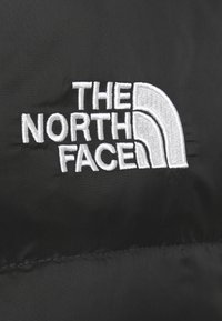 Czarna tkanina z haftowanym białym logo "THE NORTH FACE" z stylizowanym wzorem półkuli, gładką teksturą i trwałym przeszyciem.