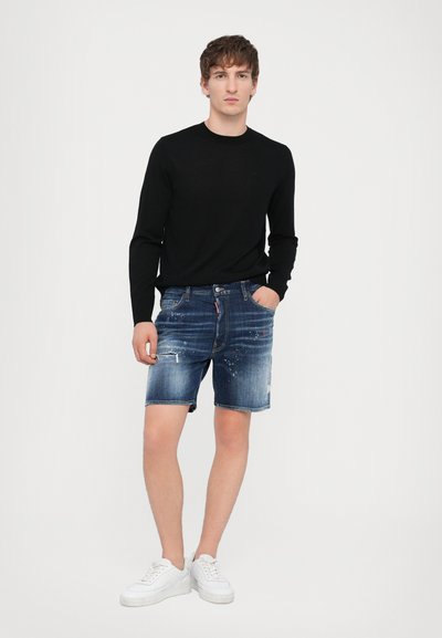 Chemise noire à manches longues associée à un short en denim déchiré bleu foncé, avec des accents bleu clair et des baskets blanches. Design simple.