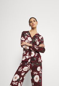Floral pajama set in burgundy with white and black flowers. Features a collared shirt and matching pants, made from soft fabric with a relaxed fit.