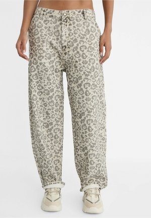 Personne portant un pantalon ample taille haute à imprimé léopard gris avec des revers, associé à des baskets épaisses beiges.