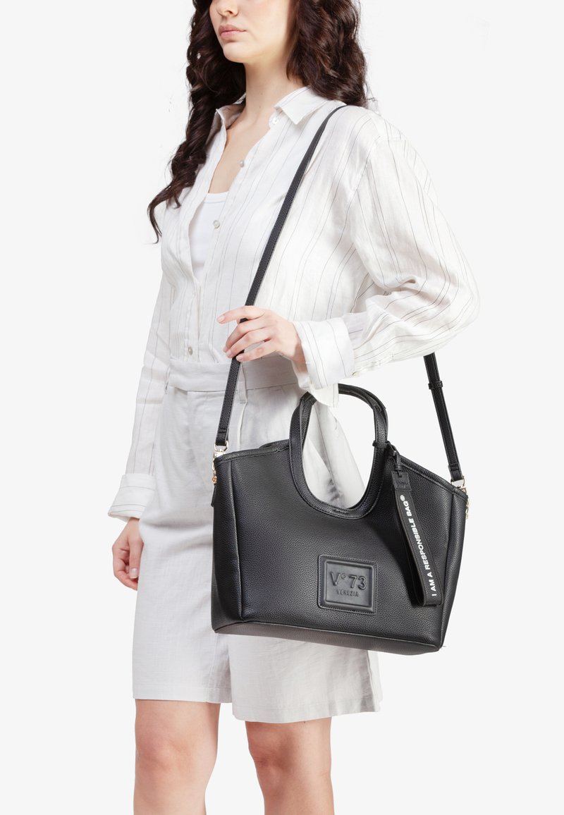 Sort læderhandbag med en tekstureret overflade, to håndtag og en aftagelig skulderrem, med et logopatch og tags.
