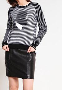 Maglione a righe bianco e nero con maniche raglan e un design grafico, abbinato a una gonna aderente in pelle nera con zipper laterale.